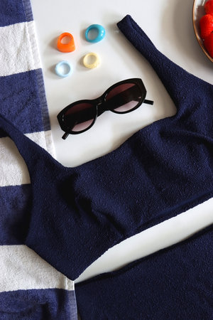 Navy swimsuit, striped beach towel, sunglasses, colorful rings and plate with berries. Top view.の写真素材