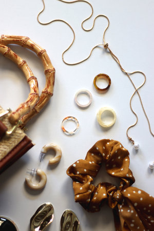 Wicker purse, sunglasses, scrunchie, lipstick and various gold and neutral jewelry on white...