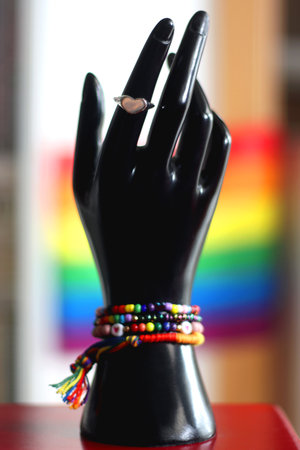 Hand figurine with colorful rainbow bracelets and heart shaped ring. Pride flag in the background. Pride month concept, selective focus.の写真素材