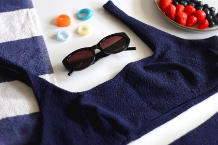 Navy swimsuit, striped beach towel, sunglasses, colorful rings and plate with berries. Selective focus.の写真素材
