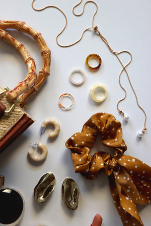 Wicker purse, sunglasses, scrunchie, lipstick and various gold and neutral jewelry on white...