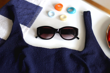Navy swimsuit, striped beach towel, sunglasses, colorful rings and plate with berries. Selective focus.の写真素材