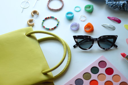 Green bag, various colorful jewelry, sunglasses, hair accessories and colorful make up on white...
