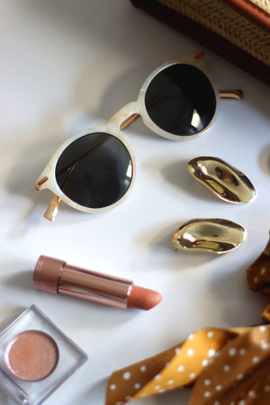 Wicker purse, sunglasses, scrunchie, lipstick and various gold and neutral jewelry on white background. Selective focus.の写真素材