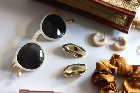 Wicker purse, sunglasses, scrunchie, lipstick and various gold and neutral jewelry on white background. Selective focus.の写真素材