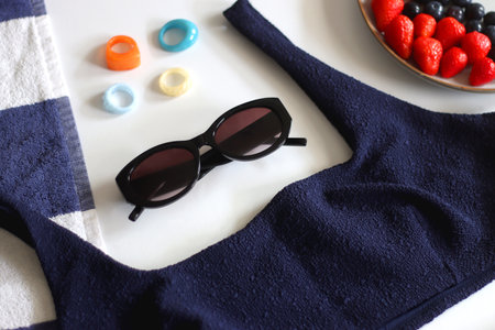 Navy swimsuit, striped beach towel, sunglasses, colorful rings and plate with berries. Selective focus.の写真素材