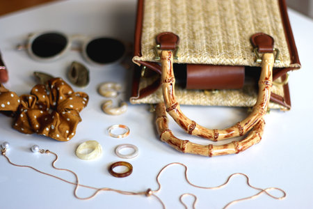 Wicker purse, sunglasses, scrunchie, lipstick and various gold and neutral jewelry on white background. Selective focus.の写真素材