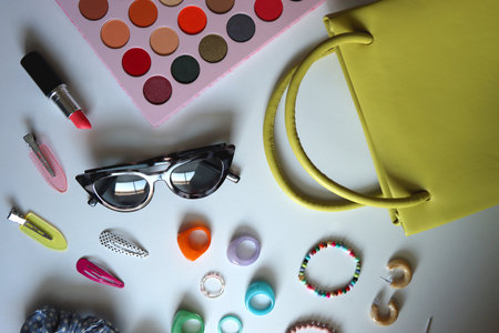 Green bag, various colorful jewelry, sunglasses, hair accessories and colorful make up on white...