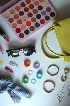 Green bag, various colorful jewelry, sunglasses, hair accessories and colorful make up on white...