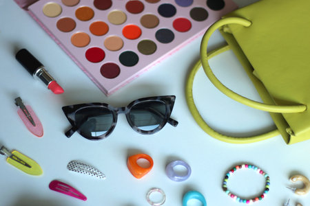 Green bag, various colorful jewelry, sunglasses, hair accessories and colorful make up on white background. Selective focus.の写真素材