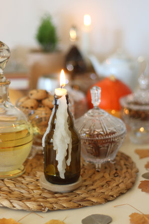 Lit candles, cookies, chocolate, nuts, tea, wine, pumpkins, books, reading glasses and autumn leaves on the table. Autumnal hygge at home. Selective focus.の写真素材