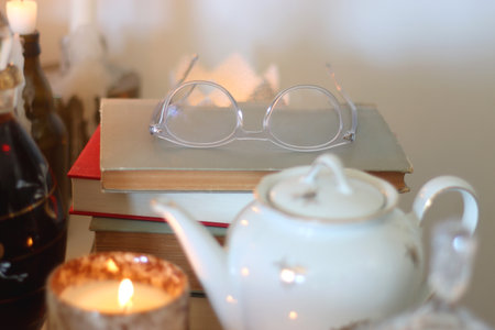 Lit candles, books, reading glasses, and a teapot on the table. Cozy atmosphere at home. Selective focus.の写真素材