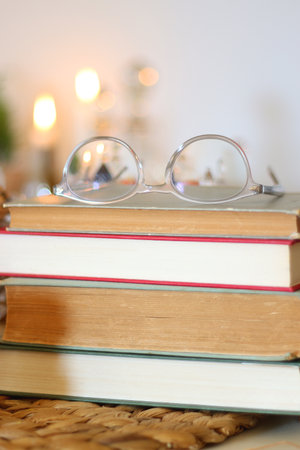 Stack of books with reading glasses on top and lit candles in the background. Selective focus.の写真素材
