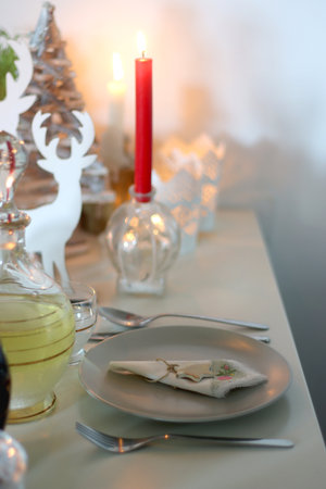 Table set for Christmas meal, with plates, wine, decorations and lit candles. Selective focus.の写真素材