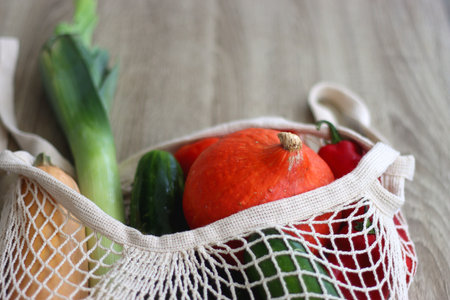 Mesh bag with various healthy vegetables on wooden background. Selective focus.