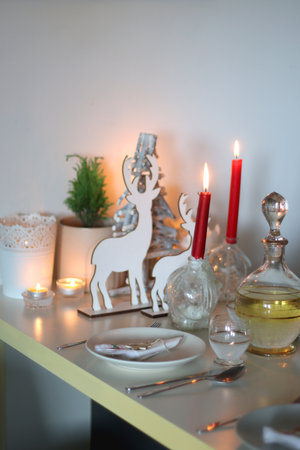 Table set for Christmas meal, with plates, wine, decorations and lit candles. Selective focus.の写真素材