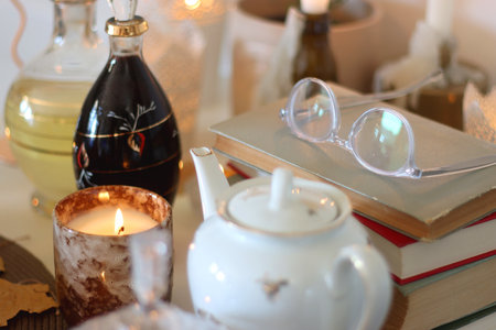 Lit candles, cookies, chocolate, nuts, tea, wine, pumpkins, books, reading glasses and autumn leaves on the table. Autumnal hygge at home. Selective focus.の写真素材