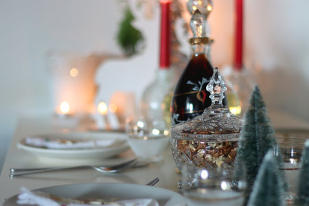 Table set for Christmas meal, with plates, wine, decorations and lit candles. Selective focus.の写真素材
