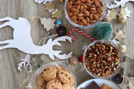 Various Christmas decorations, cookies, chocolate and nuts on wooden background. Flat lay.