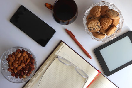 Notebook, pen, tablet, phone, coffee and snacks on white background. Top view.の写真素材