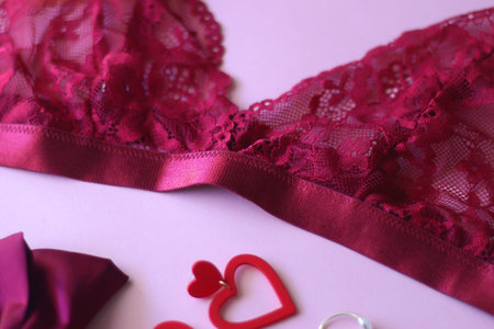 Red lace bralette, hairbow, heart shaped earrings, golden ring, red lipstick and nail polish on pink...