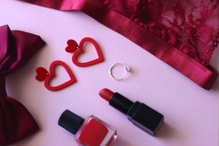 Red lace bralette, hairbow, heart shaped earrings, golden ring, red lipstick and nail polish on pink...