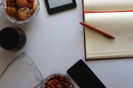 Notebook, pen, tablet, phone, coffee and snacks on white background. Top view.