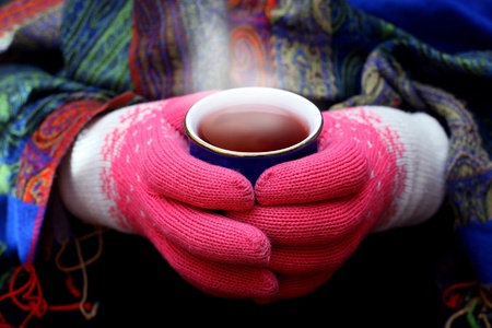Two hands in woolen gloves holding hot cup of teaの写真素材