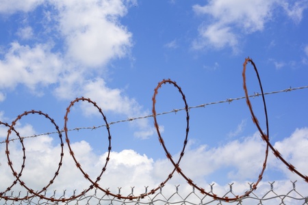 Barbed wire against sunny sky and cloudsの写真素材