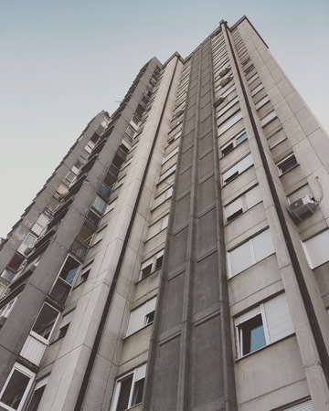 Gray concrete high-rise city housing skyscraper with numerous apartment windows reaching the pale-blue skyの写真素材