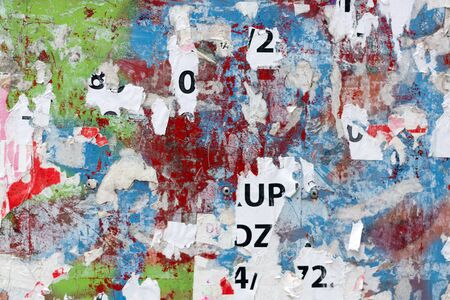 Grungy flat wall surface covered with pealed paper and red, green and blue spray paintの写真素材