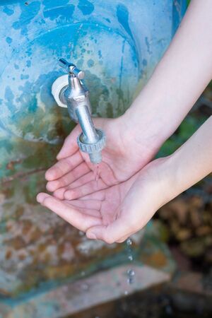 Closeup of two female palms under clear clean cold fresh stream of water from silver and blue stone fountain tapの写真素材