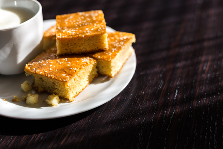Close-up view of fresh baked corn bread with cheese and cup of yogurt in white plate on wooden tableの写真素材