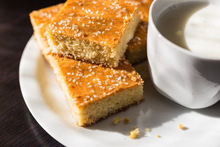 Close-up view of fresh baked corn bread with cheese and cup of yogurt in white plate on wooden tableの写真素材