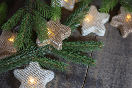 Christmas card with light star garland and fir branches oh the old wooden background. Empty space for text. Winter holidays concept.の写真素材