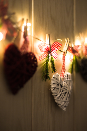 Christmas greeting card with place for your text. Decoration with hanging hearts and fir branches with lights on wooden background.の写真素材