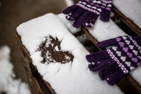 Heart drawn in the snow on a wooden bench and winter gloves. Valentine's background concept.の写真素材