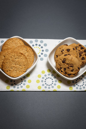 Two different kind of cookies, oatmeal and chocolate chip cookies in the white bowls. Top view flat lay background with space for text.の写真素材