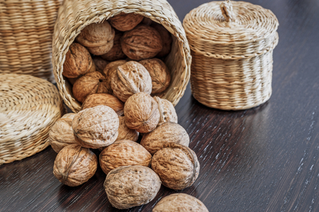 Whole walnuts in basket and scattered on a dark wooden table, space for text. Healthy food concept.の写真素材