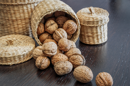 Whole walnuts in basket and scattered on a dark wooden table, space for text. Healthy food concept.の写真素材