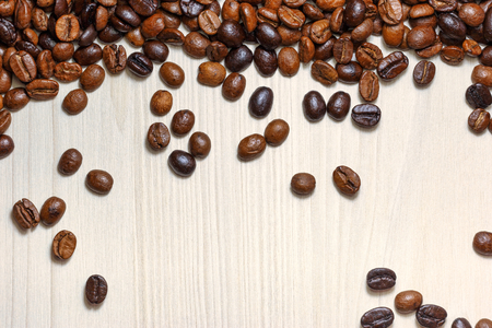 Roasted coffee beans scattered on a light wooden table, top view.