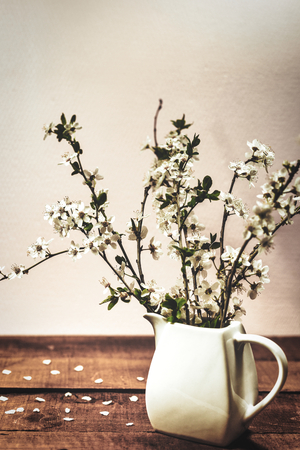 White vase with spring blossom branches on a wooden table. Vintage background with copy space.の写真素材