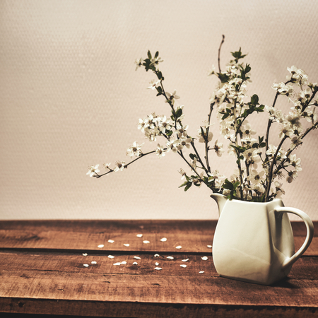 White vase with spring blossom branches on a wooden table. Vintage background with copy space. Square photo.の写真素材