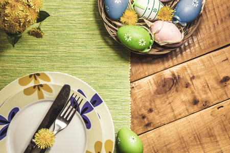 Easter table setting with colorful eggs and spring flowers on wooden table, top view. Vintage toned photo.の写真素材