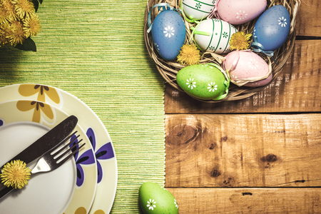 Easter table setting with colorful eggs and spring flowers on wooden table, top view. Vintage toned photo.の写真素材