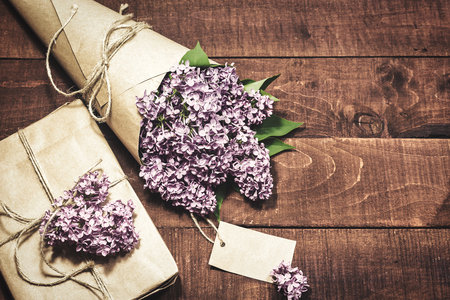 Close-up view of gift and bouquet of lilacs wrapped in kraft paper on a wooden background. Vintage toned photo.の写真素材