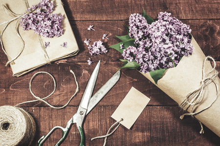 Close-up view of gift and bouquet of lilacs wrapped in kraft paper on a wooden background. Vintage toned photo.の写真素材