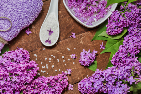 Spa and wellness composition with perfumed lilac flowers water in bowl, sea salt and towel on wooden background. Aromatherapy for relaxation, top view, flat lay.の写真素材