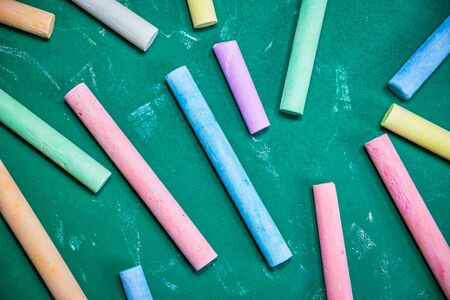 Multicolored chalks scattered on a green chalkboard, back to school concept. Top view with copy...