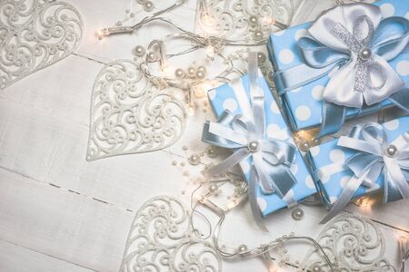 Top view of blue gift boxes with white and blue ribbon and lights decorated with pearls on white wooden background with copy space. Vintage toned photo. Christmas and New Year concept.の写真素材